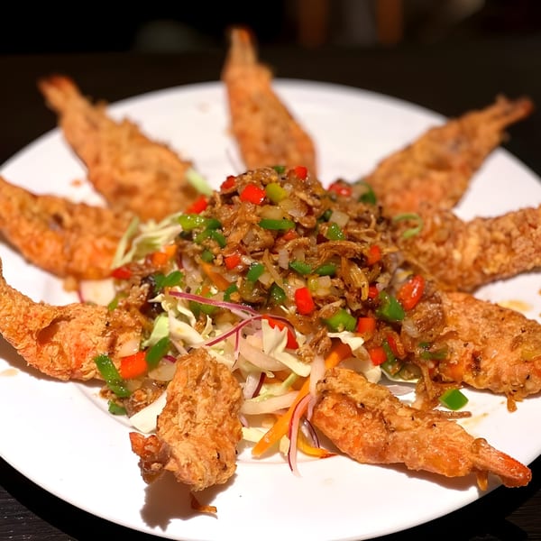 Crispy fried shrimp arranged in a circle around a colorful salad with peppers and onions.